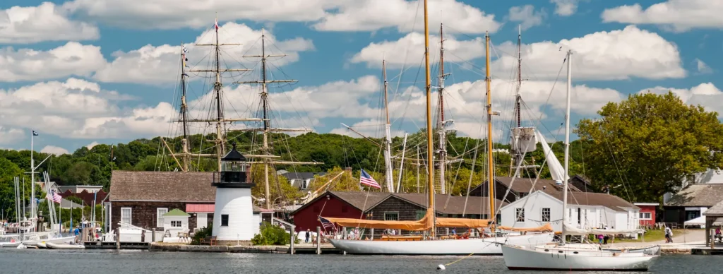 Historic Mystic Seaport Museum featuring tall ships, a lighthouse, and traditional wooden buildings along the waterfront.