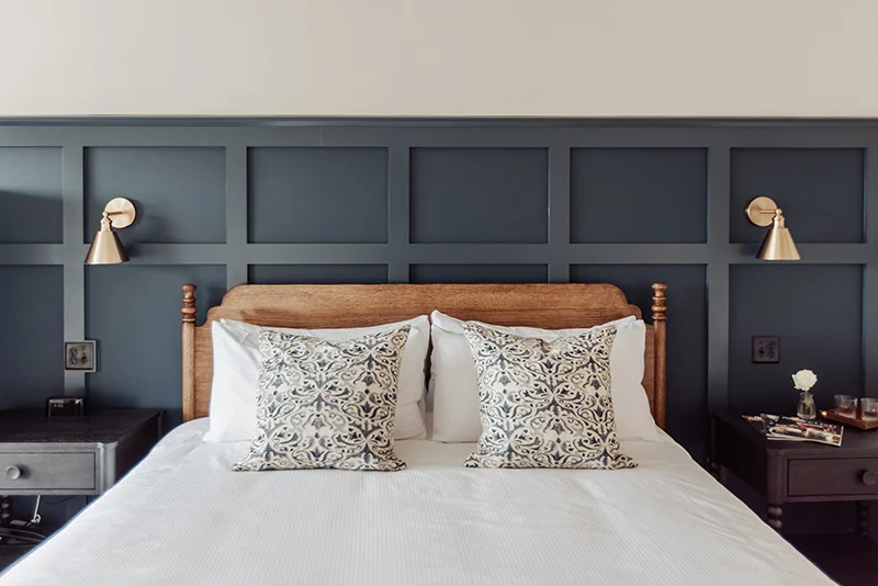 Modern bedroom featuring a wooden headboard, dark paneled accent wall, and brass wall sconces.