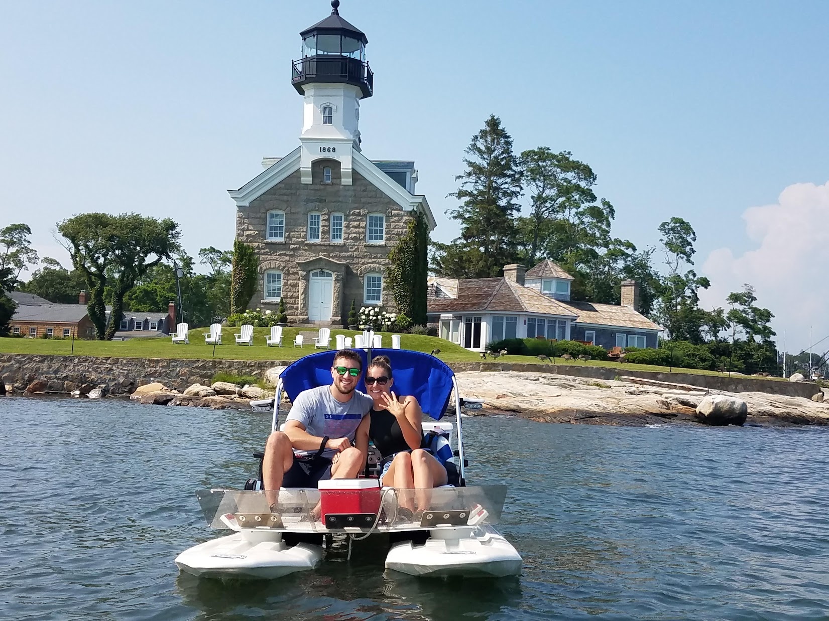 Couple showing off engagement ring on a pedal boat in front of the historic Sheffield Island Lighthouse.