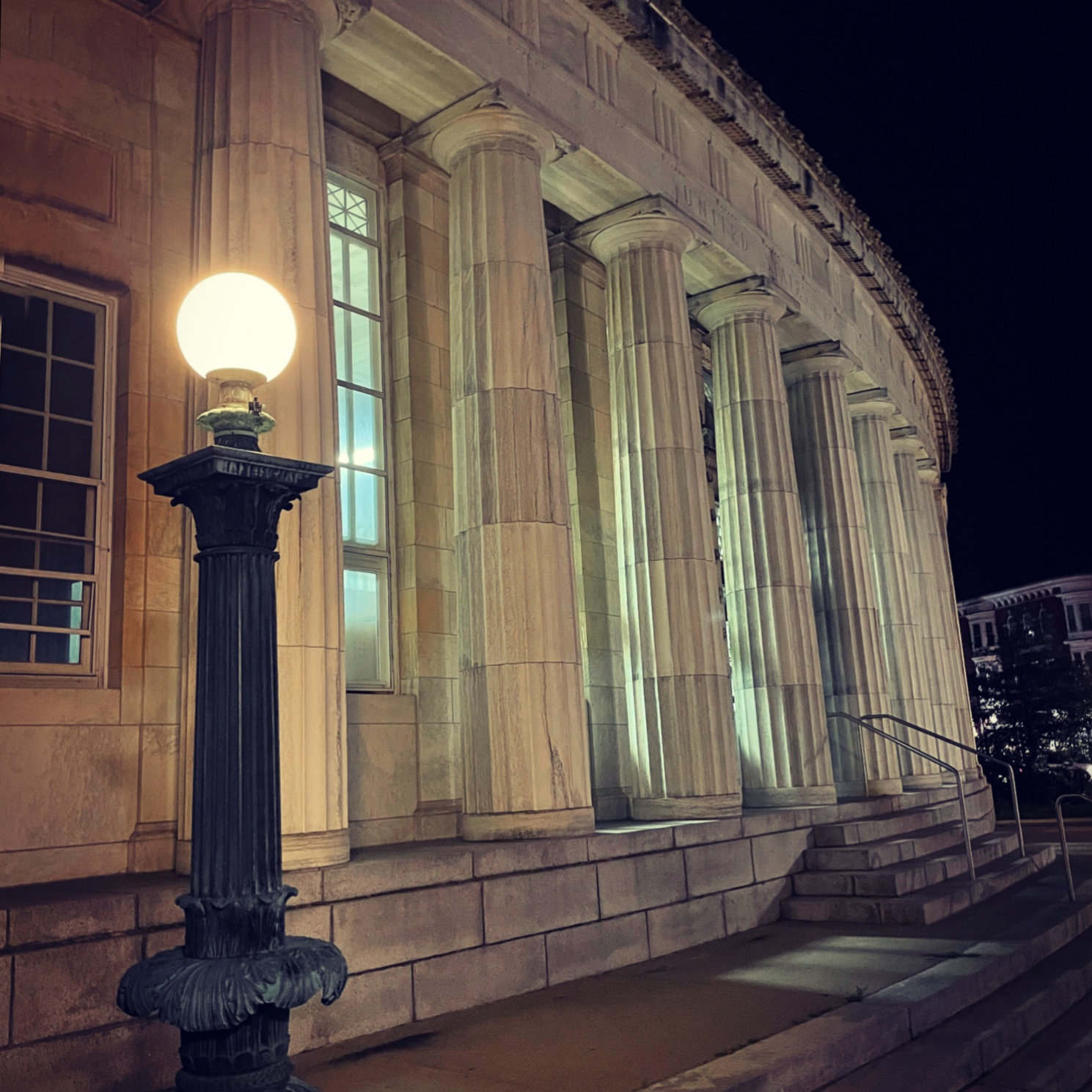 Classical stone columns of a government building illuminated by a vintage street lamp at night.