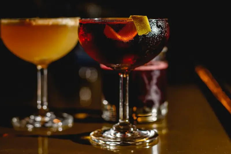 Two elegant craft cocktails in chilled coupe glasses served on a bar counter in a dimly lit setting.