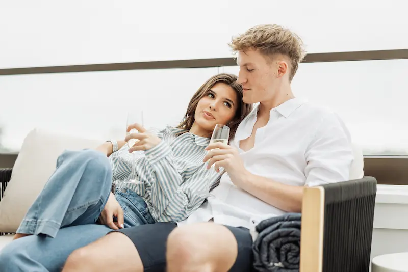 A young couple sits closely together on an outdoor patio while holding glasses of champagne.