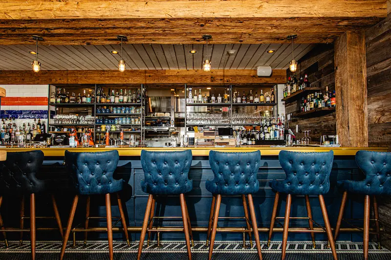 One of the most outstanding Mystic Restaurants is the Shipwright's Daughter. Featuring a rustic bar interior with tufted blue leather stools, wooden ceiling beams, and a well-stocked liquor shelf.