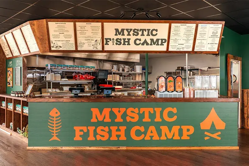 The interior of Mystic Fish Camp restaurant, featuring a rustic service counter and menu board.