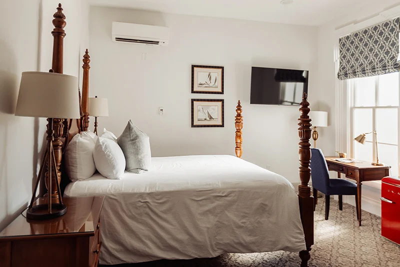 Cozy hotel room featuring a four-poster bed, wooden desk, and nautical decor in a bright, modern interior.