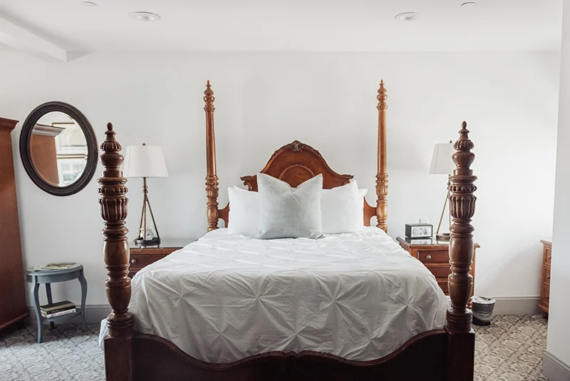 Elegant bedroom featuring a traditional wooden four-poster bed with white bedding against a clean, neutral wall.