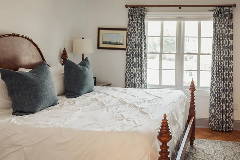 Cozy bedroom featuring a wooden spindle bed frame, white textured bedding, and blue patterned curtains.