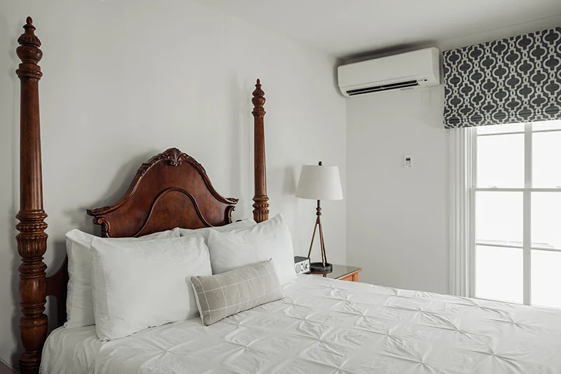 Cozy bedroom interior featuring a dark wood four-poster bed, white bedding, and modern wall-mounted air conditioner.