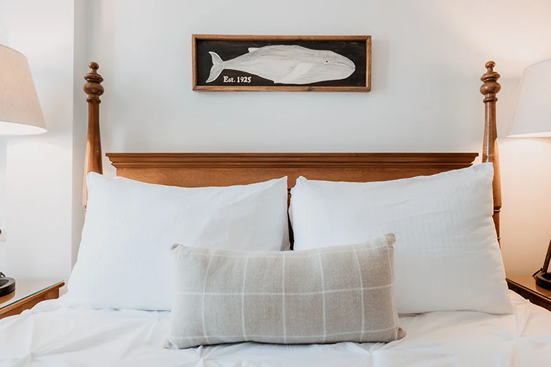Cozy bedroom with wooden headboard, white bedding, and coastal-themed whale wall art.
