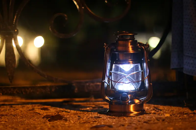 A glowing metal lantern sits on a dark ground at night with blurred background lights.