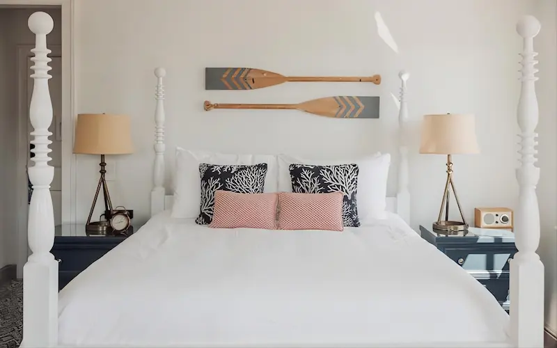 Coastal-style bedroom with a white four-poster bed, patterned throw pillows, and decorative oars on the wall.