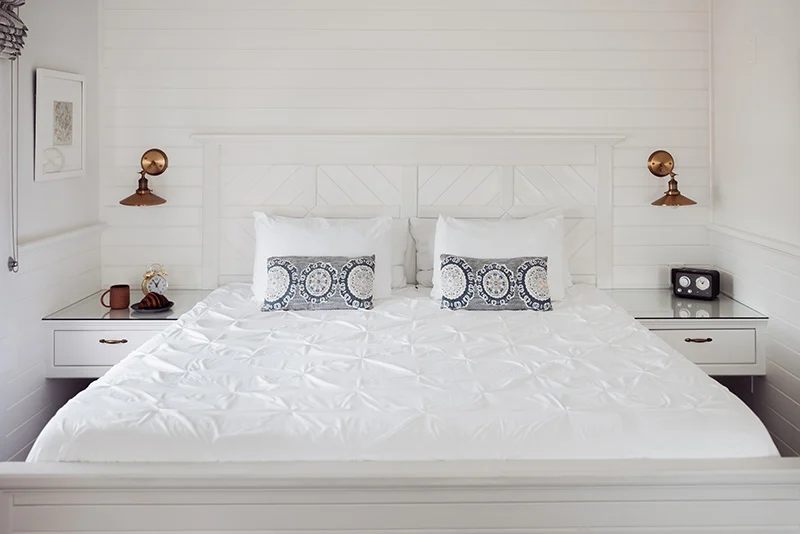 Bright, modern bedroom featuring white shiplap walls, a tufted bed, and matching floating bedside tables.
