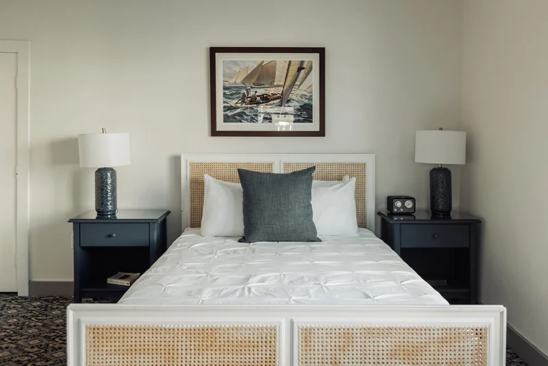 Cozy bedroom featuring a white cane bed frame, dark blue nightstands, and nautical wall art.