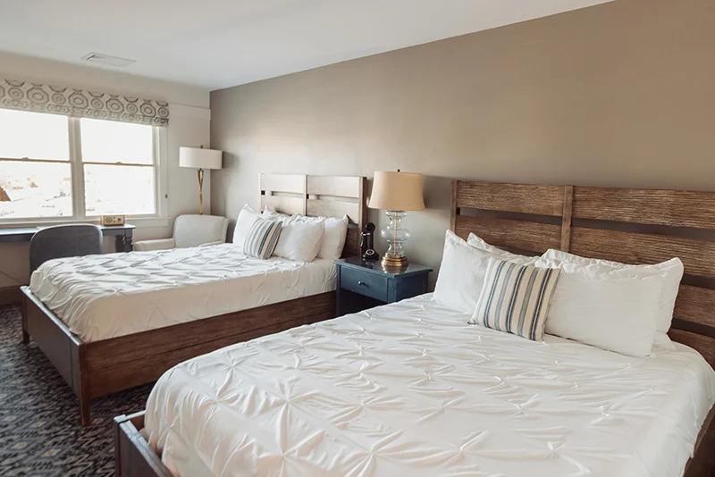 Cozy hotel bedroom with two queen beds, rustic wooden headboards, and neutral decor.