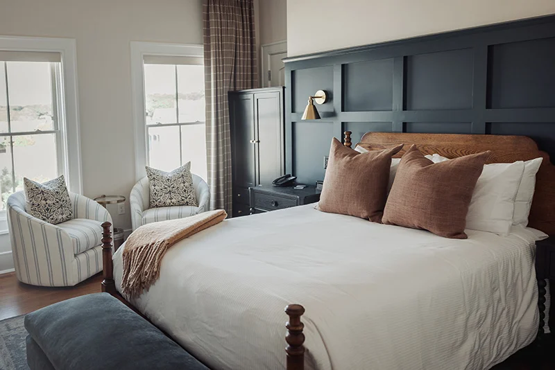 Modern farmhouse bedroom featuring a dark navy panel accent wall, wooden bed frame, and cozy neutral seating area.