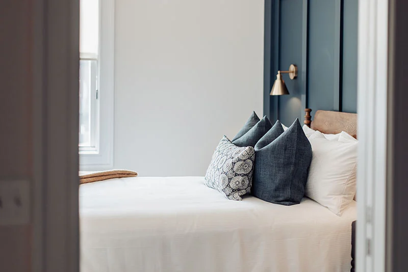 Modern bedroom featuring a dark blue paneled accent wall, brass wall sconce, and stylish layered decorative pillows.