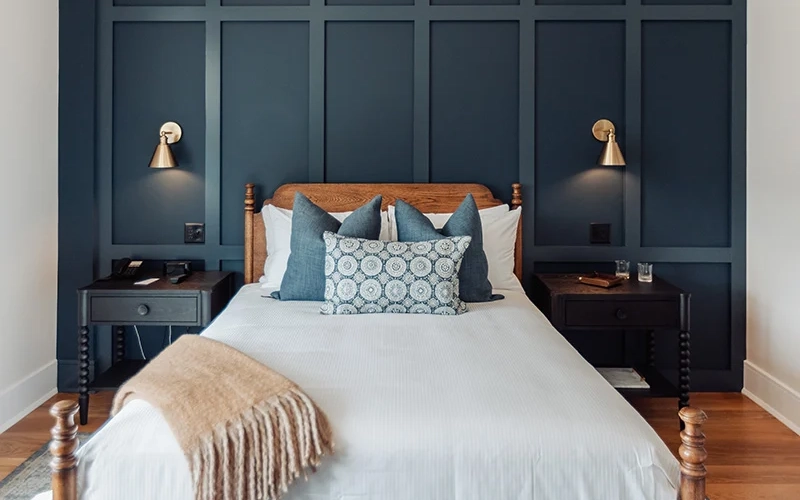 Modern bedroom featuring a dark navy paneled accent wall, wooden bed frame, and gold wall sconces.