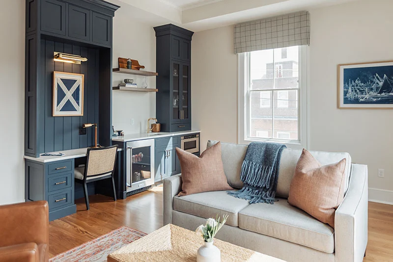Modern living room featuring a navy blue home office workstation, built-in bar, and cozy gray sofa with accent pillows.