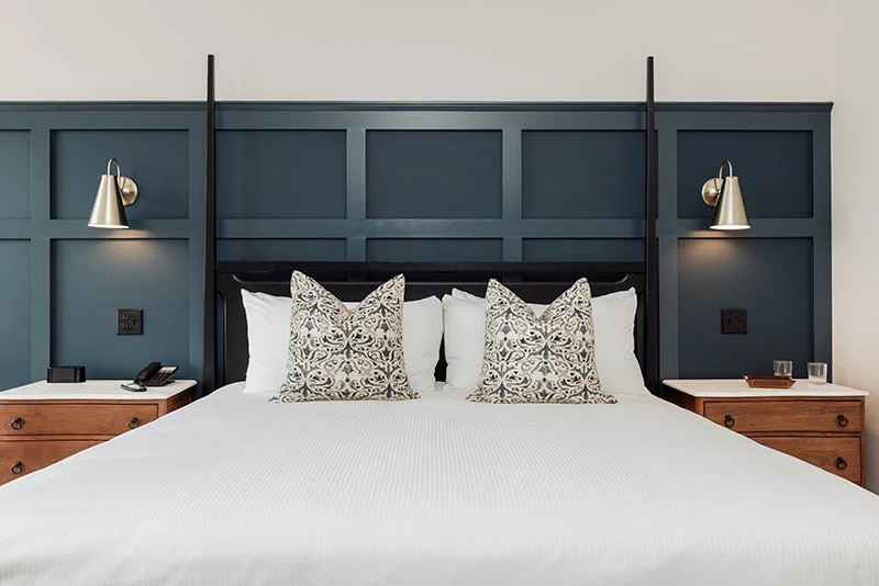 Modern bedroom with a dark blue paneled headboard wall, wooden nightstands, and elegant gold wall sconces.