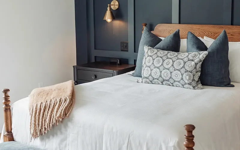 Modern bedroom interior featuring a wooden bed frame, dark navy wall paneling, and brass wall sconce lighting.