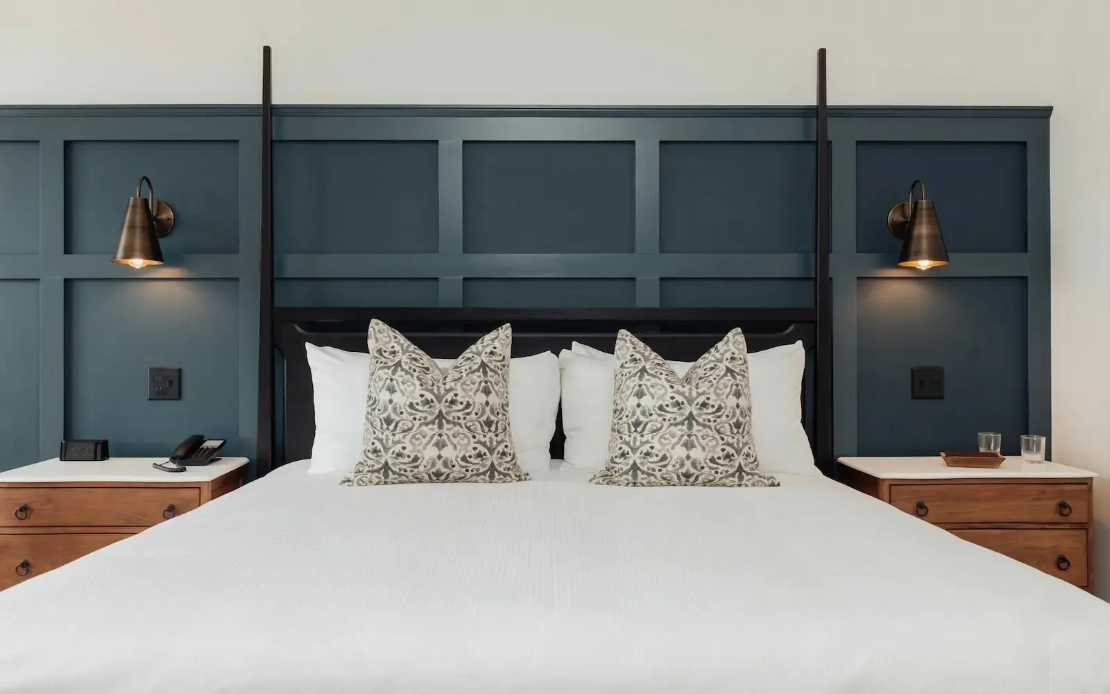 Modern bedroom featuring a dark blue paneled headboard wall, wooden nightstands, and patterned decorative pillows.