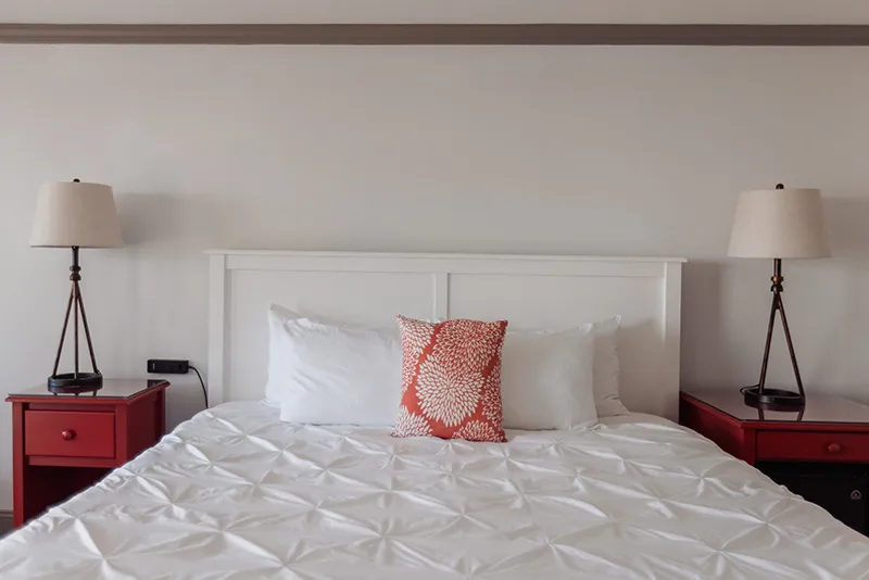 Modern white bedroom with a tufted duvet, red nightstands, and matching bedside table lamps.