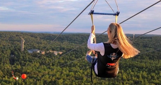 Woman enjoying a scenic zipline adventure over a vast forest canopy at sunset.
