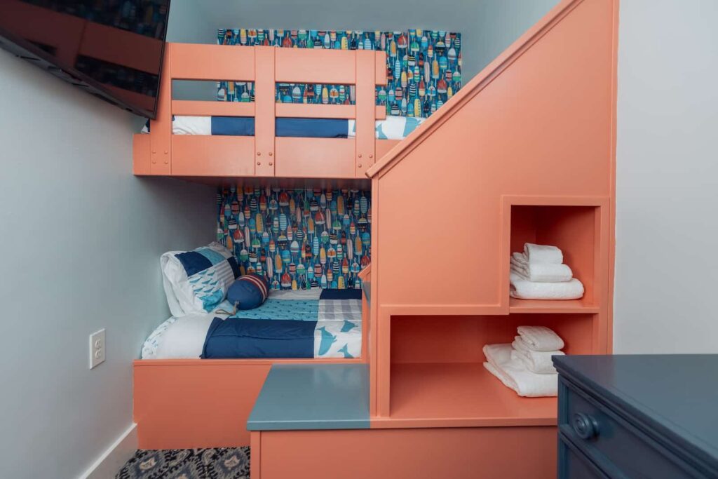 Modern coral-colored bunk bed with nautical-patterned wallpaper and integrated storage shelving in a coastal bedroom.