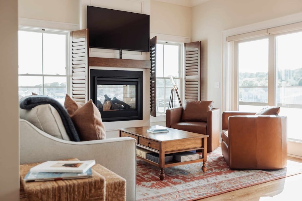 Cozy coastal living room featuring leather armchairs, fireplace, and flat-screen TV with serene window views.