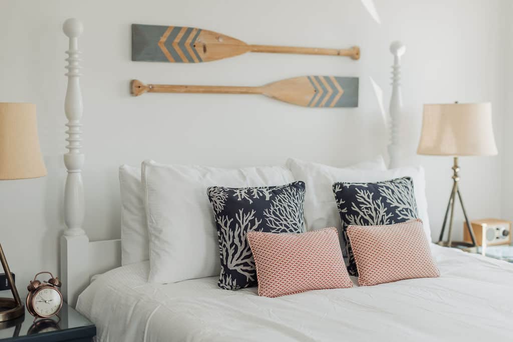Coastal bedroom featuring a white bed with coral-print pillows and decorative oars mounted on the wall.