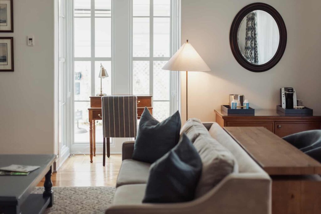 Cozy hotel room interior featuring a sofa, wooden desk, lamp, and round mirror.