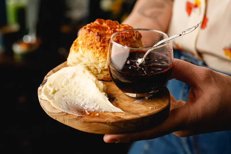 Freshly baked scone served with a smear of butter and fruit jam on a rustic wooden board.