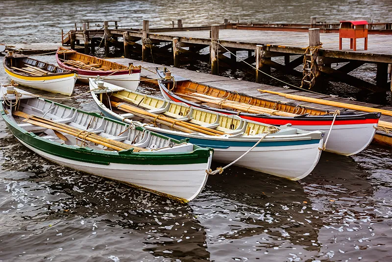 Colorful wooden rowboats moored at a wooden pier on calm water.