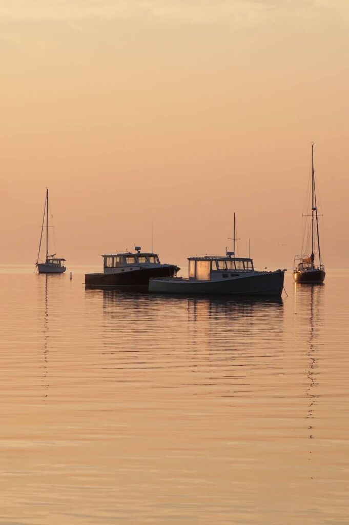 Boats float on calm, golden water during a serene sunset at sea.