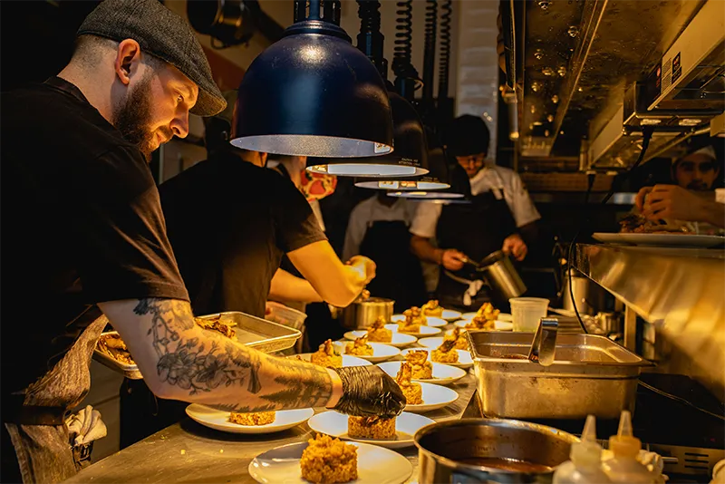 Professional chefs plating gourmet dishes in a busy, warm-lit restaurant kitchen.