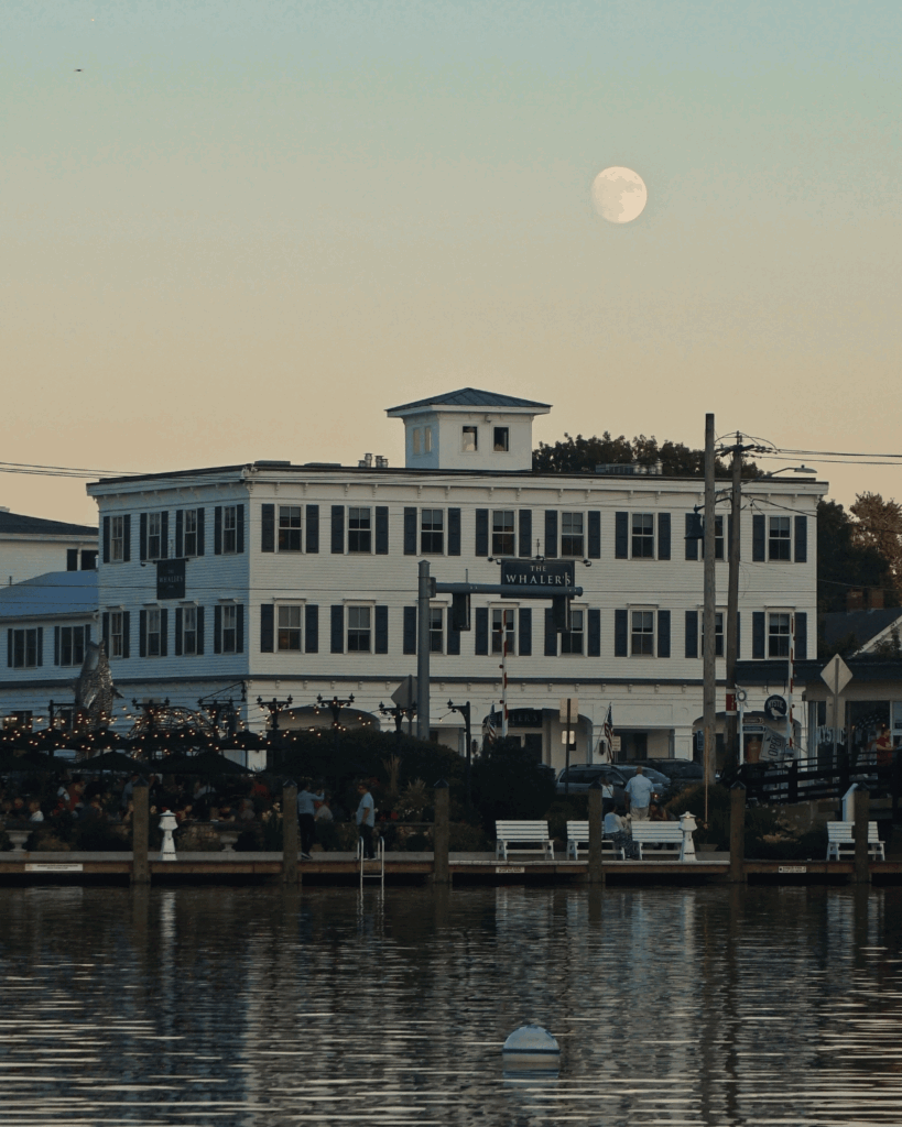 Full moon rises over The Whaler's Inn and harbor waterfront in scenic Mystic, Connecticut at twilight.
