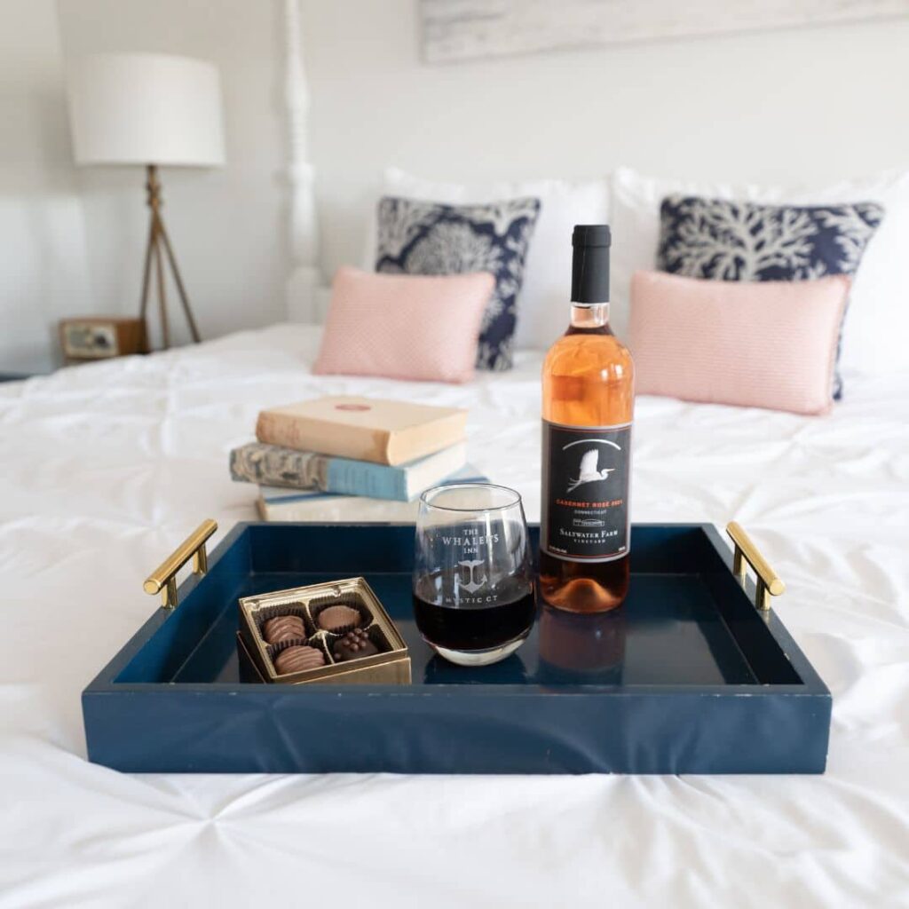 A navy blue tray with wine, chocolates, and books on a cozy hotel bed.