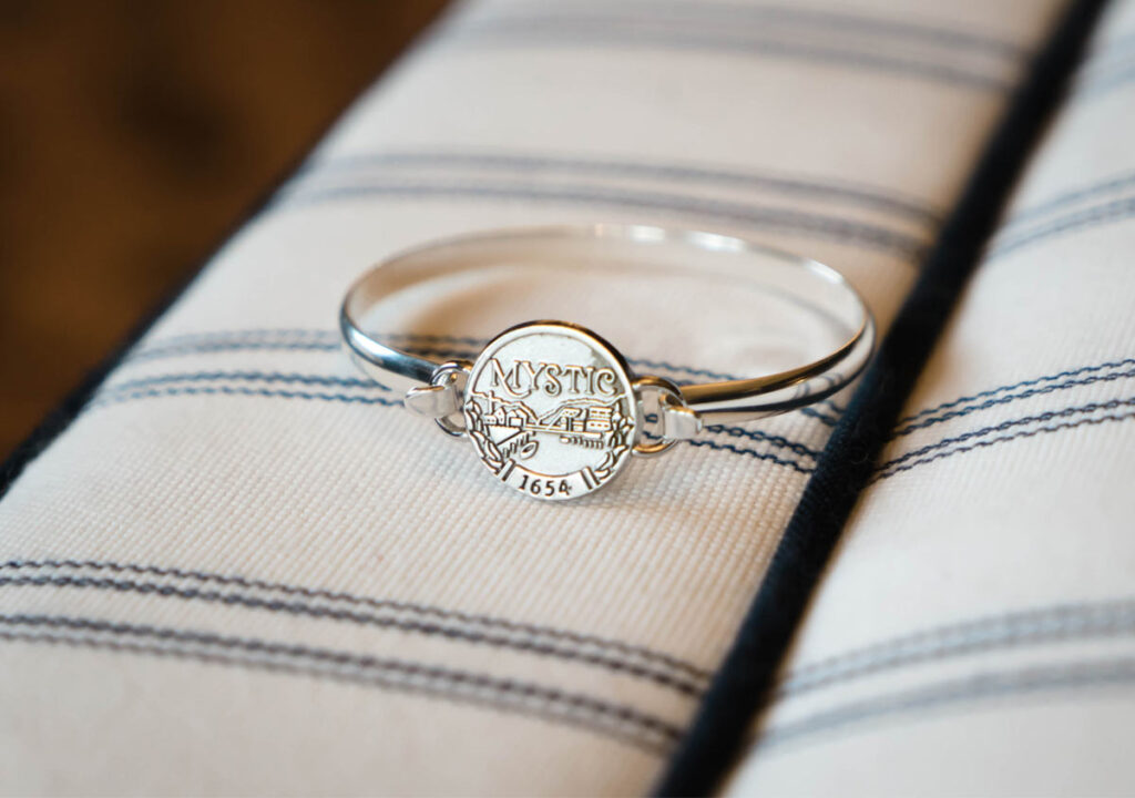 Silver bangle bracelet featuring a round Mystic 1654 charm on a striped fabric background.