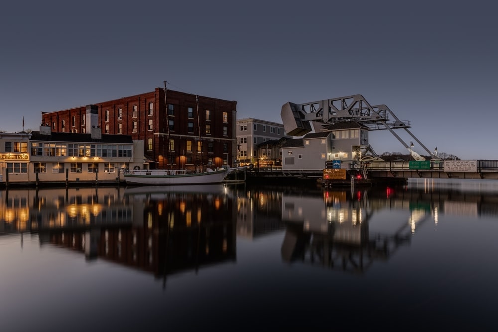 Historic waterfront buildings and a drawbridge reflected in the calm waters of Mystic, Connecticut at twilight.