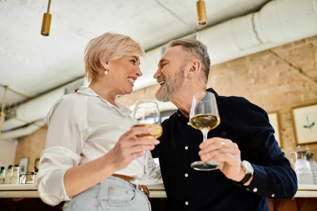 Happy middle-aged couple drinking white wine and laughing together at a bar.