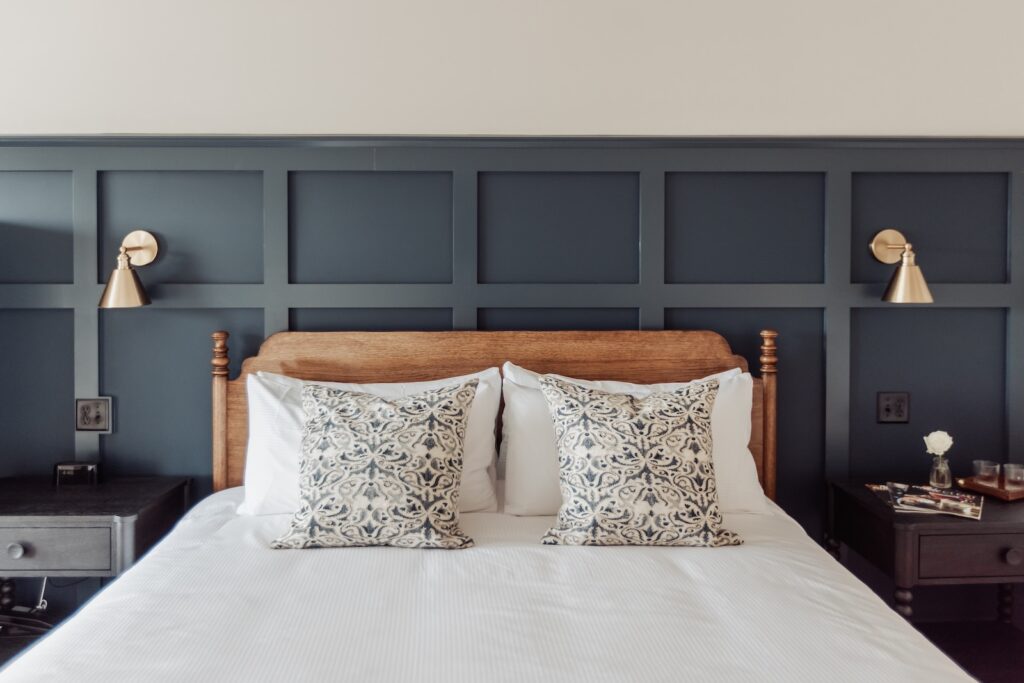 At one of the best Mystic hotels, CT, you'll find a comfortable bed against a dark blue backdrop, framed by wall sconces and nightstands and adorned with two throw pillows.