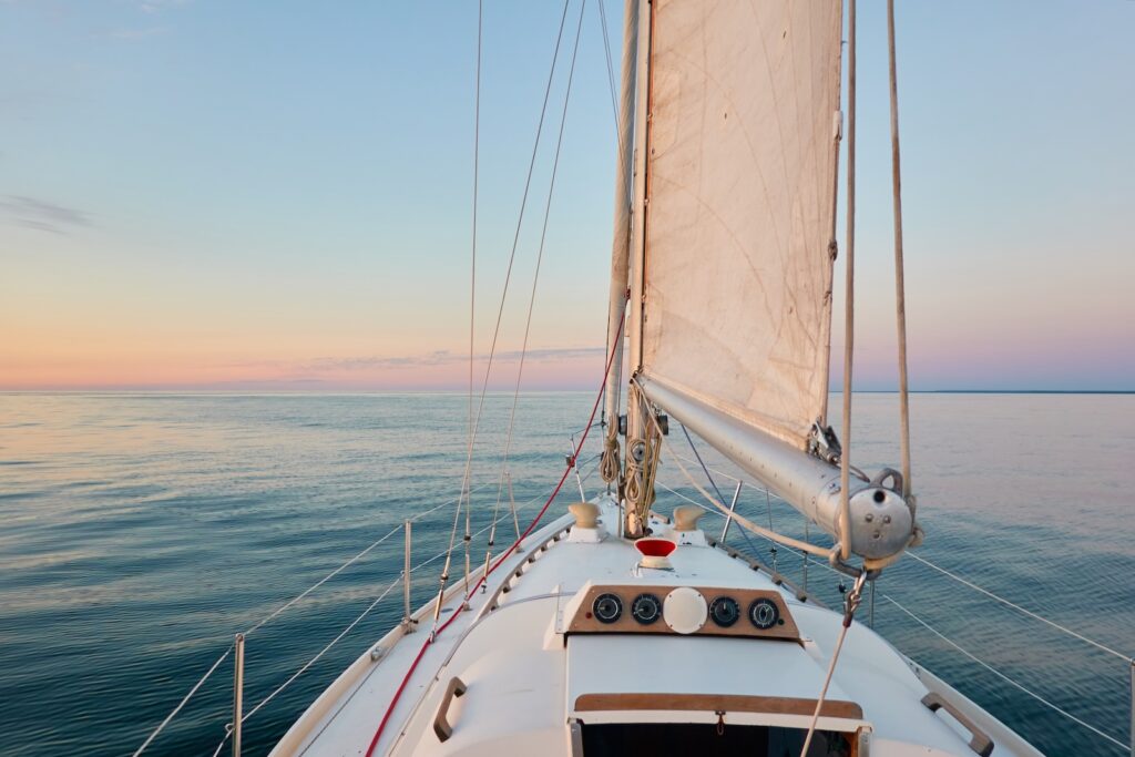 When you take a sunset cruise in Mystic, CT, with Argia Mystic Cruises, you will see blue waters against a white boat and tan sail.