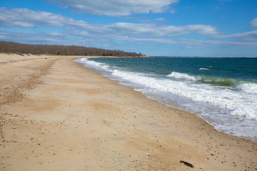 The ocean meeting the sand with trees in the background at Bluff Point State Park near Mystic, Connecticut.