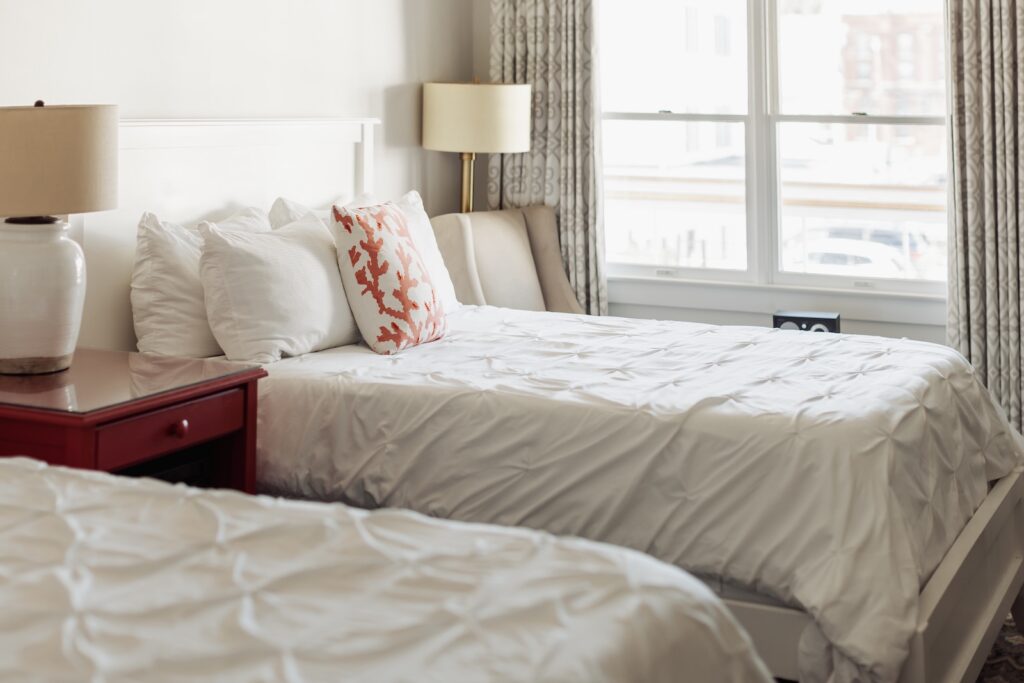 Two bed by the window with a white comforter and orange pill, what you'll find at one of the best hotels in Mystic CT.