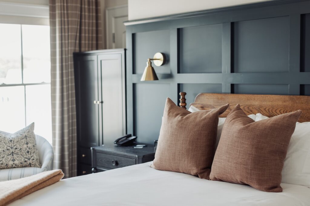 A bed with a white comforter and brown throw pillows against a blue wall, showcasing a luxury room at one of the best Mystic Connecticut hotels.