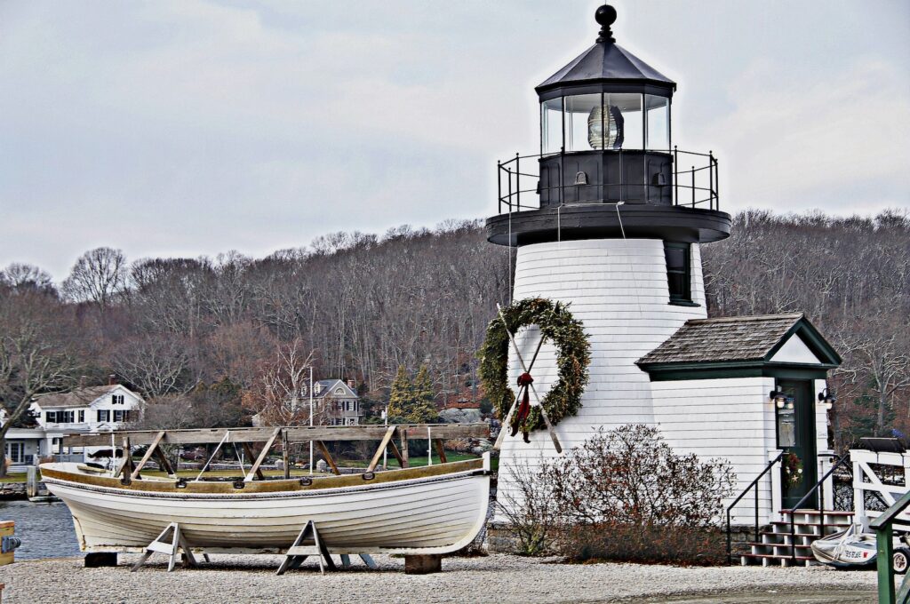A decorated lighthouse alongside a sailboat, dry docked, during Mystic Connecticut Christmas.